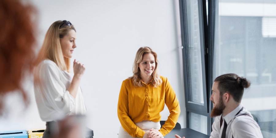 Junge Kollegen in einem Büro-Meeting: Zwei Frauen und ein Mann mit Bart unterhalten sich freundlich am Besprechungstisch.