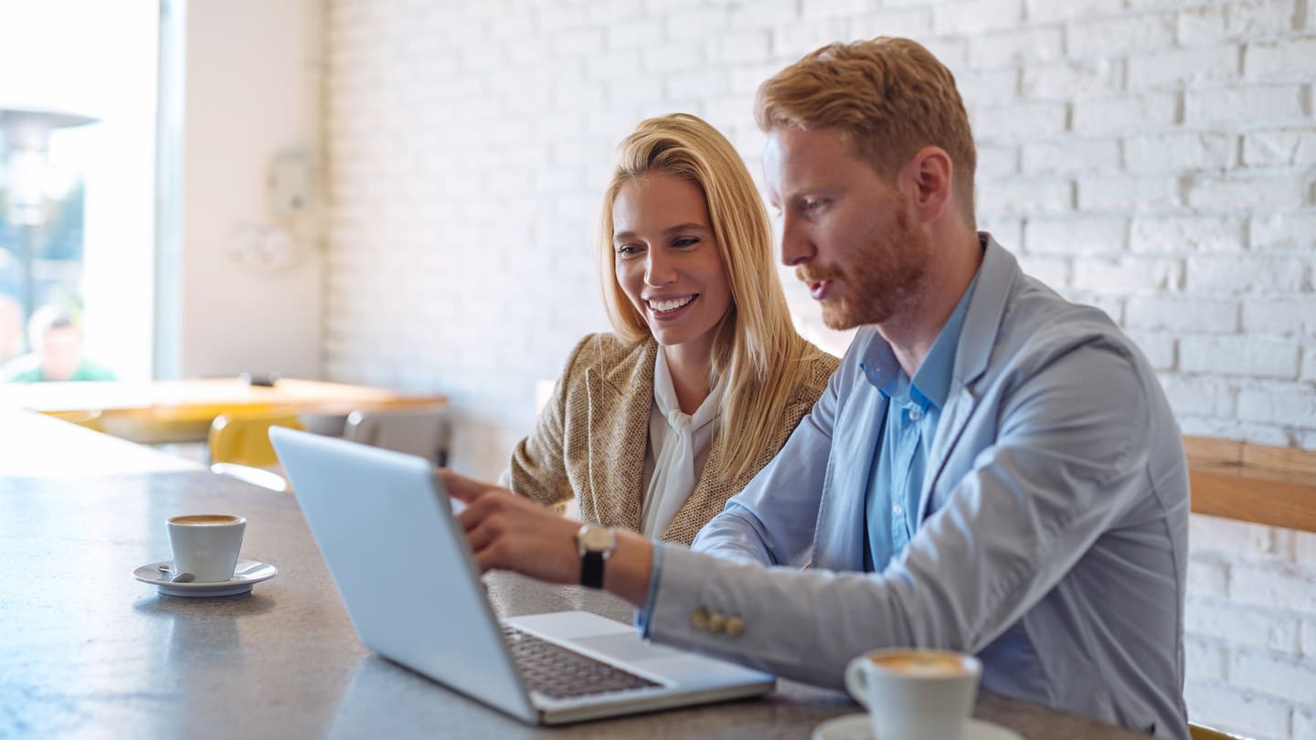A woman and a man look at digital content on a laptop in a café, a symbol of EPR access in everyday life.