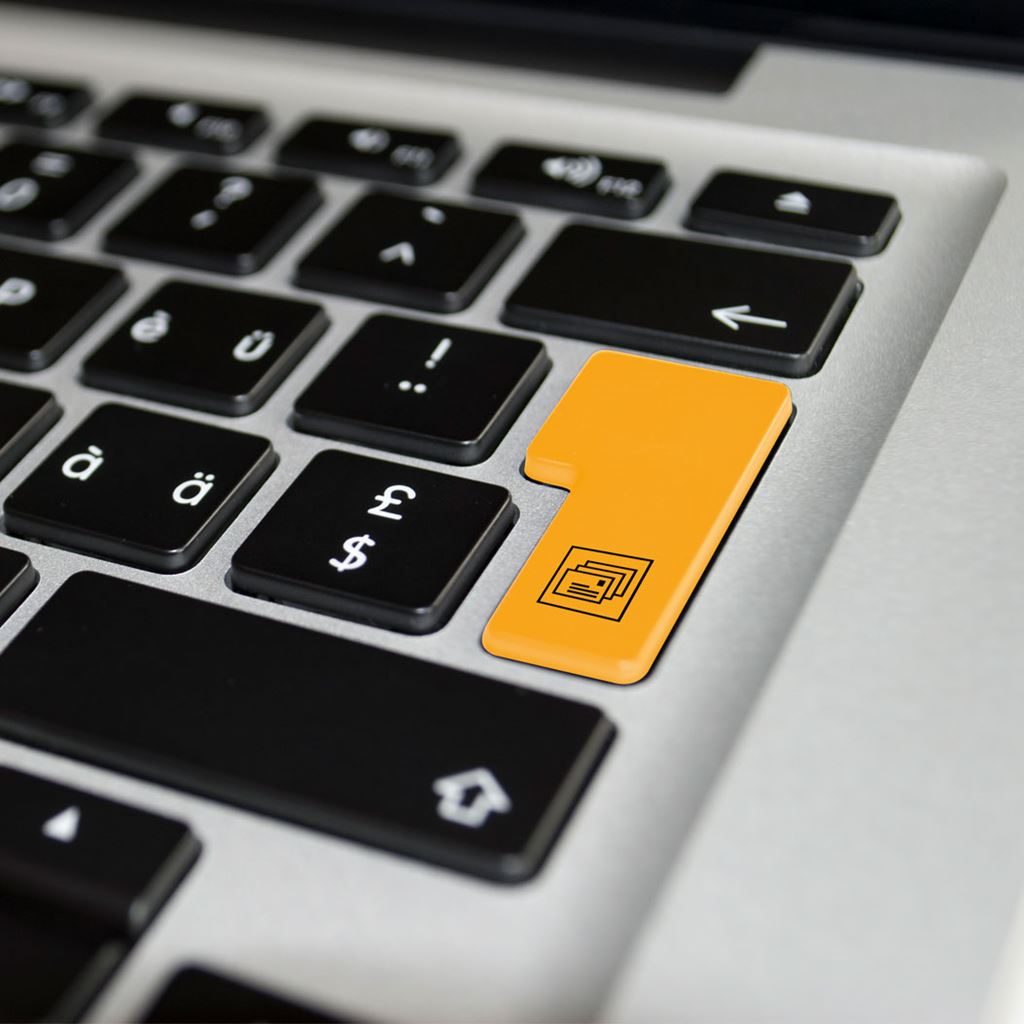 Primo piano della tastiera di un computer portatile con un vistoso tasto arancione recante il simbolo di una scheda elettorale, simbolo dell'inizio del processo di voto elettronico della Posta Svizzera.