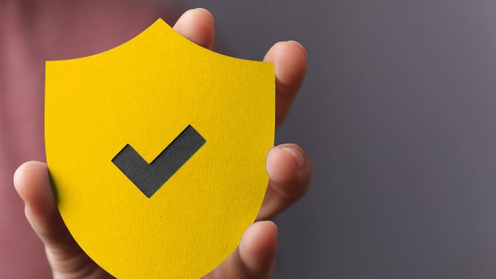 Una mano regge un cartello di carta giallo con un segno di spunta nero su sfondo grigio: un'illustrazione della sicurezza e della fiducia verificate nel sistema di voto elettronico della Posta Svizzera.