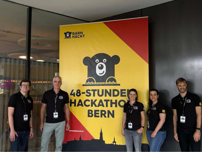 Cinque persone davanti a un banner dell’hackathon BärnHäckt di 48 ore a Berna.