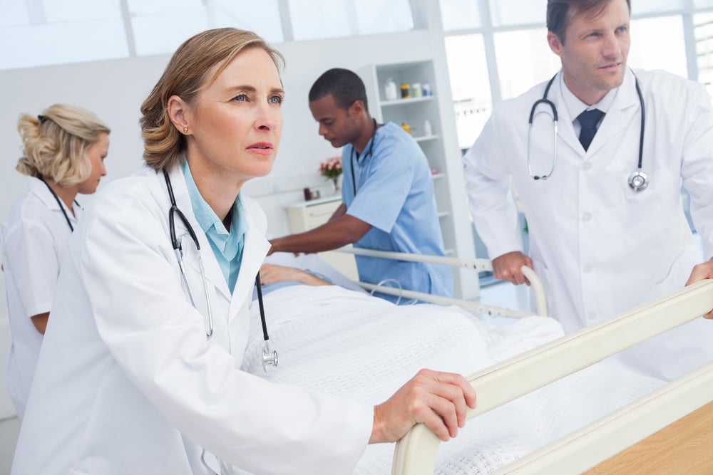 Ärzteteam im Notfalleinsatz schiebt eine:n Patient:in auf einer Trage durch den Klinikflur.