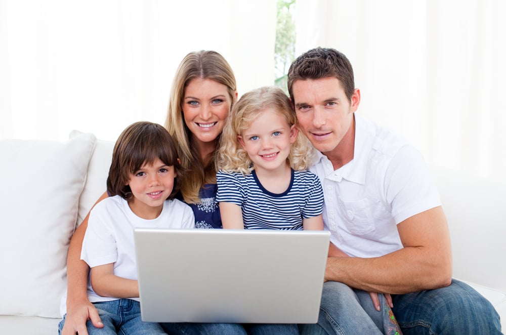 Portrait of a joyful family using a laptop sitting on sofa at home