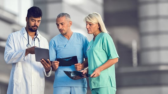 Three medical specialists are standing side by side and are deep in conversation. One holds a tablet and the other two X-rays.