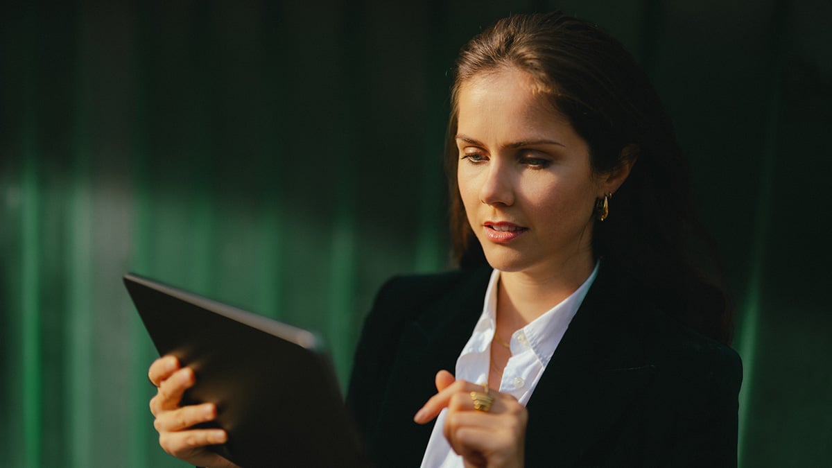 Eine Frau in Business-Kleidung blickt auf ein Tablet, das sie in der Hand hält.