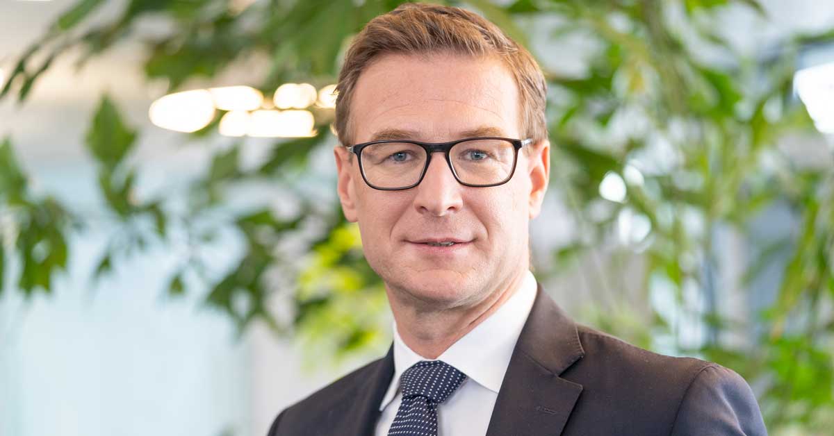 Person in einem dunklen Anzug mit weissem Hemd und gepunkteter Krawatte steht vor einem Hintergrund mit grünen Pflanzen und unscharfen Lichtelementen. Person in einem dunklen Anzug mit weissem Hemd und gepunkteter Krawatte steht vor einem Hintergrund mit grünen Pflanzen und unscharfen Lichtelementen.