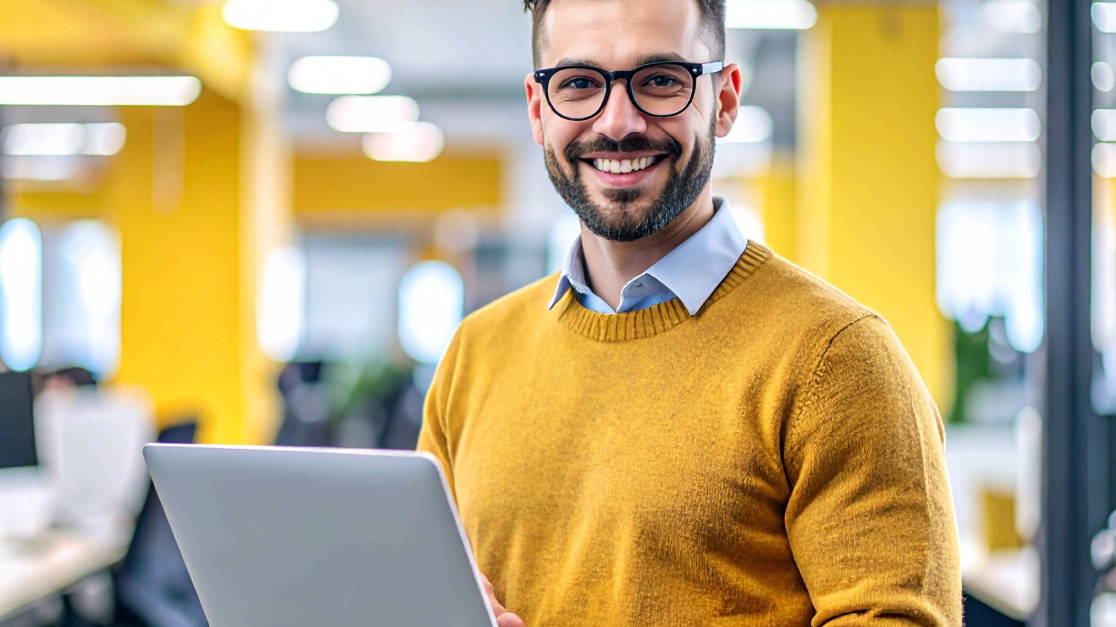 A man with a beard and glasses holding a notebook in his hand. He looks at the camera with a laugh.